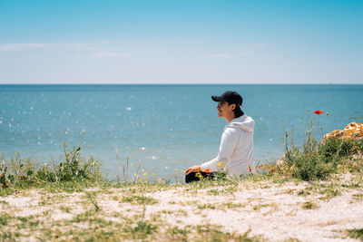 Man sitting on beach looking at sea against sky