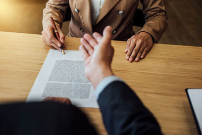 Midsection of businessman signing contract while colleague gesturing on table