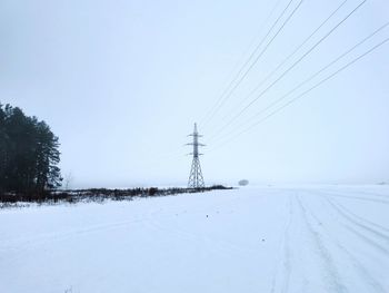 Electricity pylon on snow covered landscape against sky