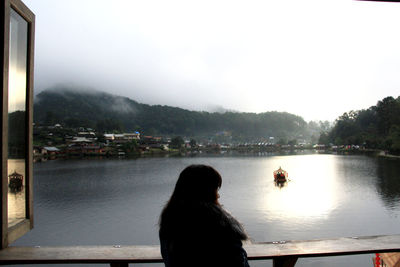 Rear view of woman looking at lake against sky