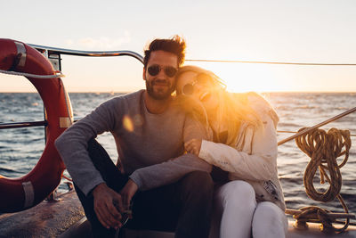 Portrait of smiling couple sitting in boat on sea against sky