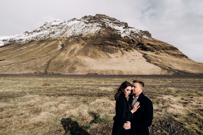 Young couple standing on mountain against sky