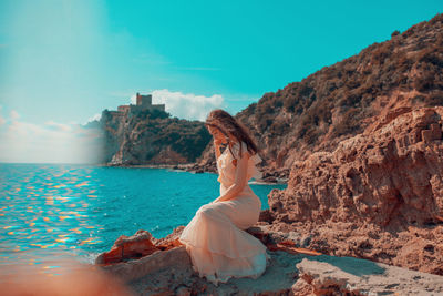 Woman sitting on rock by sea against sky