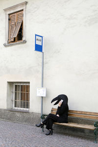 Female in crow costume talking on mobile phone while sitting at bus stop