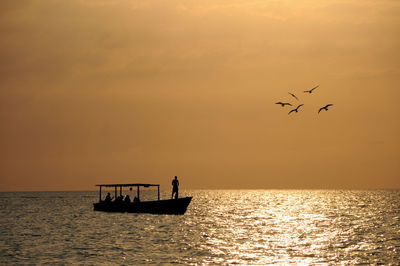 Silhouette birds flying over sea against sky during sunset