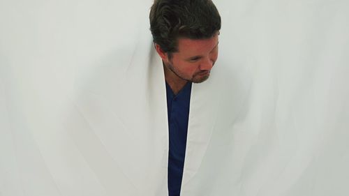 Young man looking away while standing against wall