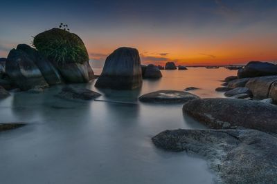 Rocks on shore against sky during sunset