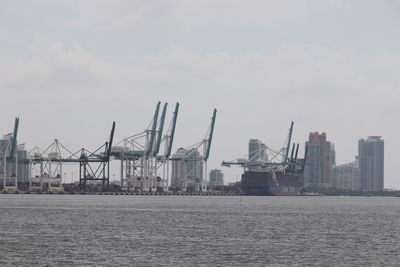Cranes at harbor against sky in city