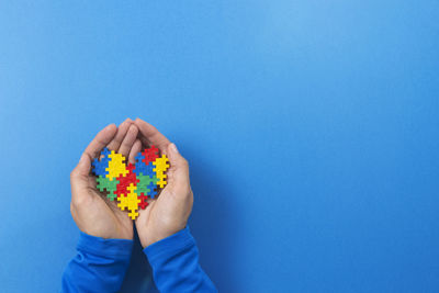 Low section of person holding multi colored candies against blue background