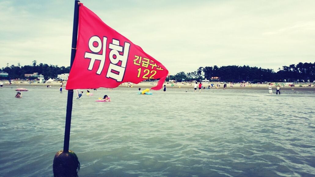 water, sea, sky, text, flag, beach, western script, guidance, patriotism, communication, red, cloud - sky, identity, waterfront, shore, men, day, lifestyles, rippled