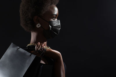 Close-up portrait of young woman holding cigarette against black background