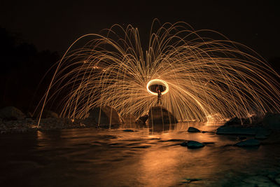 Illuminated ferris wheel by river against sky at night