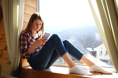 Young woman looking away while sitting on window sill