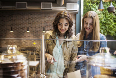 Smiling friends pointing at display cabinet while standing in cafe