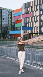 Full length portrait of man standing on railing against buildings in city