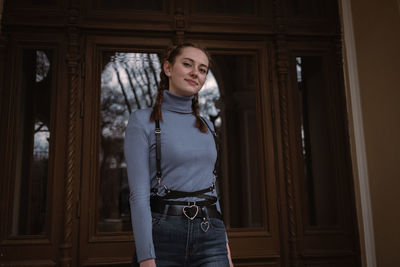 Portrait of smiling young woman standing against door