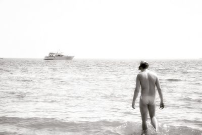 Rear view of shirtless man standing on sea against clear sky