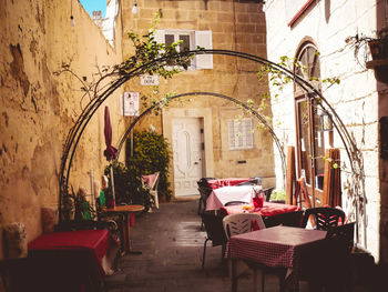 Empty chairs and tables in alley amidst buildings in city