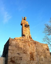 Low angle view of statue against blue sky and building