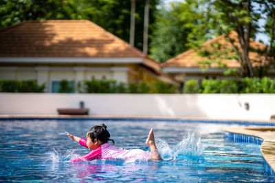 Little girl with pink swim suit jumping into swimming pool in summer.