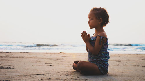 Full length of girl sitting on beach against clear sky