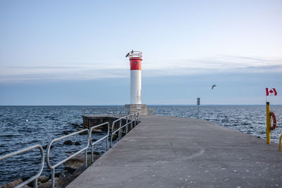 Lighthouse on pier by sea against sky