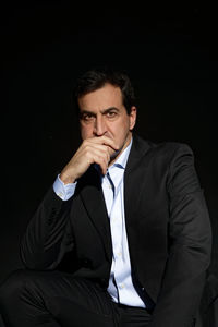 Mid adult man sitting against black background