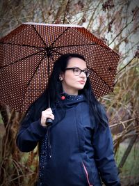 Thoughtful young woman in warm clothing holding umbrella during winter