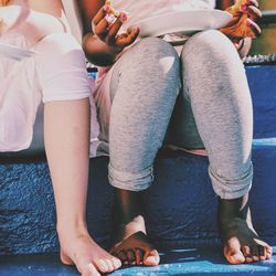 Low section of female friends having food while sitting on blue steps