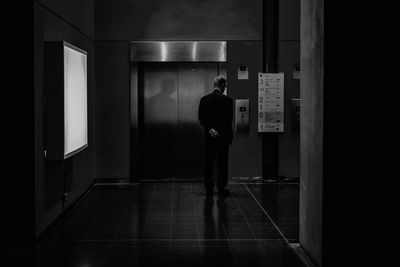 Rear view of man standing in illuminated room