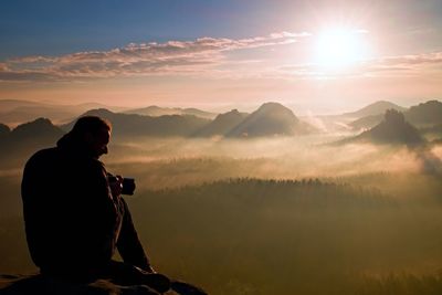 Photographer silhouette above a clouds sea, misty mountains