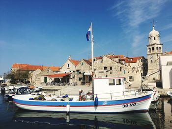 Sailboats moored on harbor by buildings against blue sky