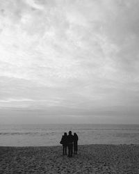 Rear view of couple standing on beach against sky