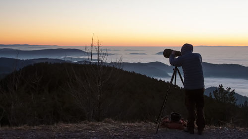 Man photographing on shore against sky during sunset