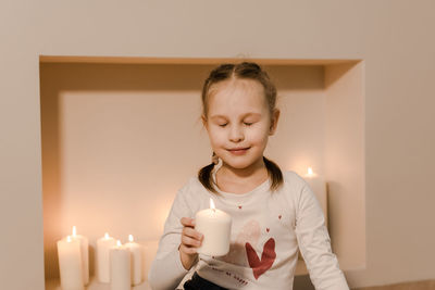 A child by the fireplace holds a burning candle