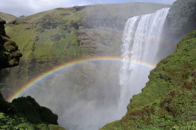 Scenic view of waterfall against rainbow in sky