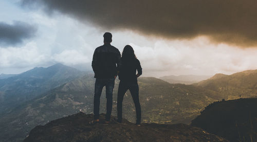 Rear view of man and woman standing on rock while looking at landscape