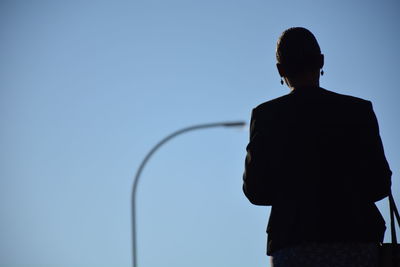 Rear view of man standing against clear blue sky