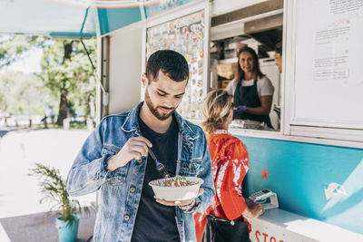Young man eating fresh tex-mex in bowl against food truck