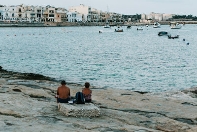 Rear view of men sitting on rock in sea