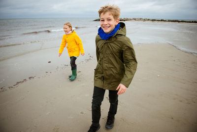 Full length portrait of smiling boy walking with sister at beach