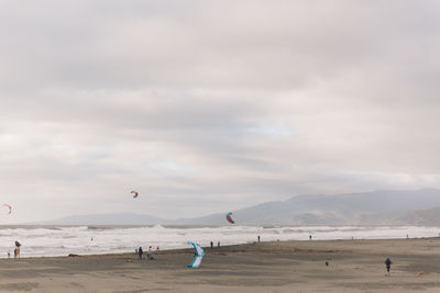 People at beach against cloudy sky