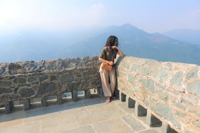 Woman looking away while standing by retaining wall