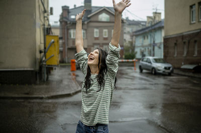 Happy woman with arms raised enjoying rain in city