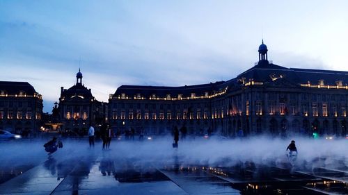 People by fountain against illuminated place de la bourse