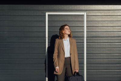 Young businesswoman with eyes closed in front of black corrugated wall on sunny day