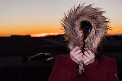 Close-up of woman wearing fur coat against sky during sunset