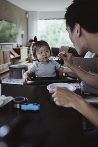 Cropped image of father feeding baby son at home