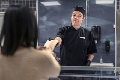 Confident young male butcher giving package to female customer