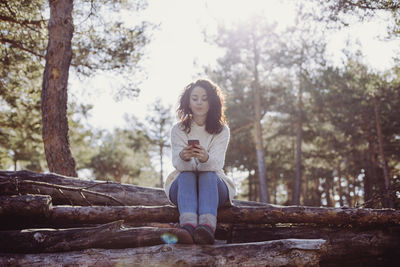 Full length of young woman sitting against trees